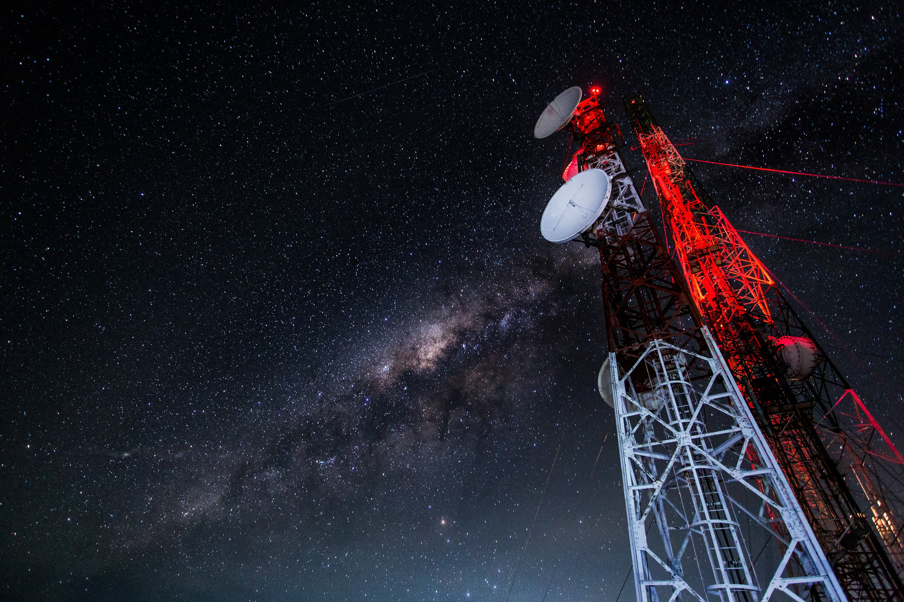 A red-lit radio tower with a glowing beacon against a star-filled night sky