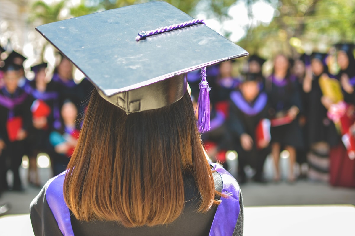 A graduate in cap and gown facing a crowd at commencement